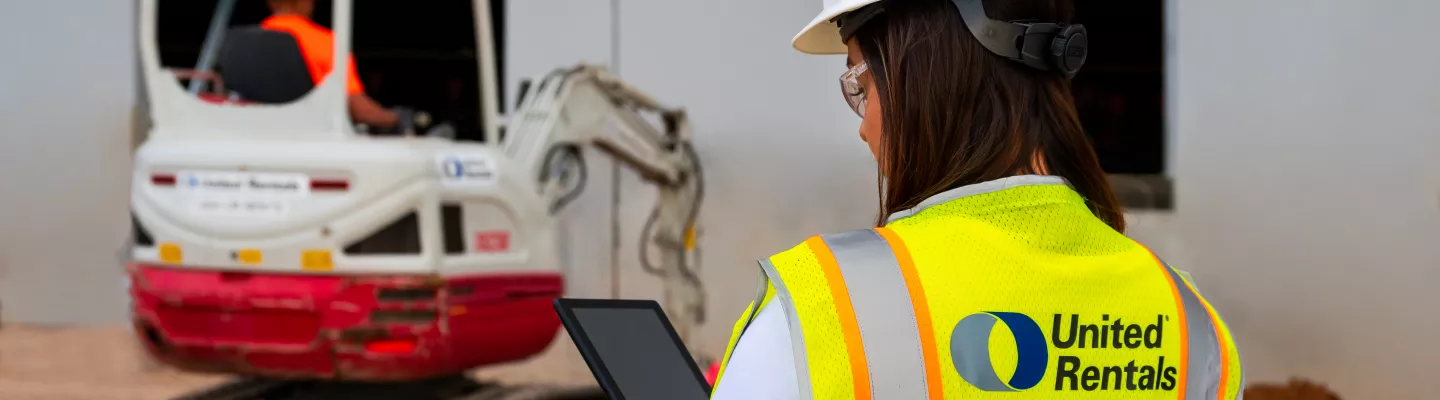 femme sur un chantier tenant un iPad près d’une chargeuse à direction à glissement