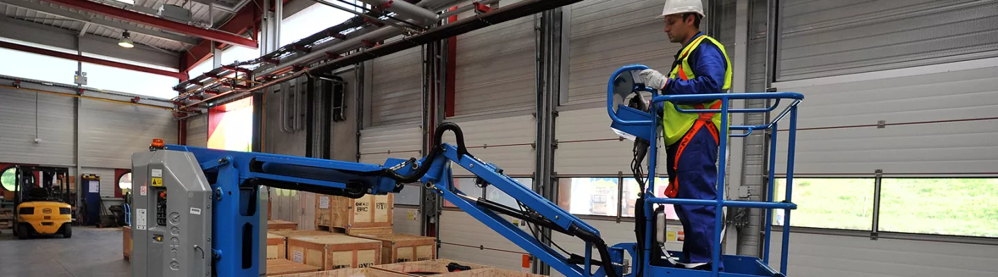 Travailleur sur une nacelle élévatrice électrique à l’intérieur d’un entrepôt