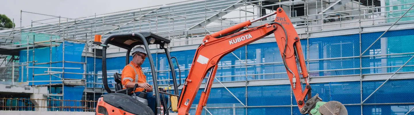 Homme utilisant une excavatrice pour excaver un terrain près de barrières de sécurité sur un chantier de construction actif.