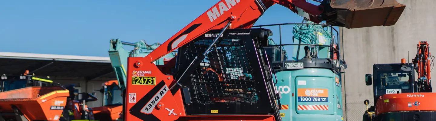 Homme utilisant une chargeuse à pneus déplaçant de la terre sur un chantier de construction avec des barrières de sécurité visibles en arrière-plan.