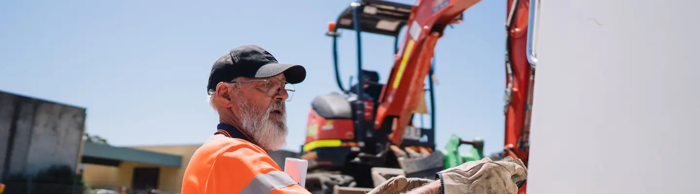 Travailleur debout à côté d’un camion-chargeuse sur un chantier de construction, inspectant ou ajustant l’équipement près des barrières de sécurité.