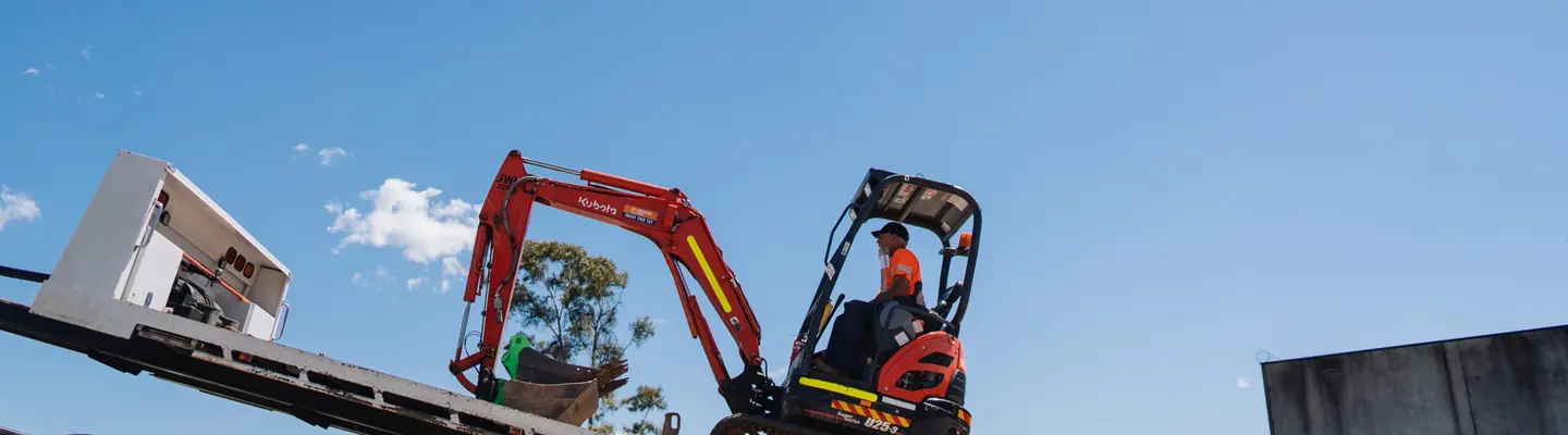 Un homme utilisant un véhicule à remorque à chenilles sur un chantier de construction, transportant des matériaux sur des terrains accidentés.