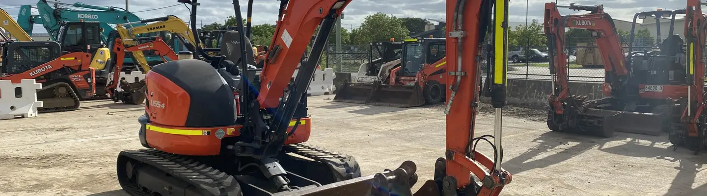 Gamme d’excavatrices d’occasion exposées dans une cour de construction, avec des panneaux de sécurité et des barrières marquant la zone de visualisation.