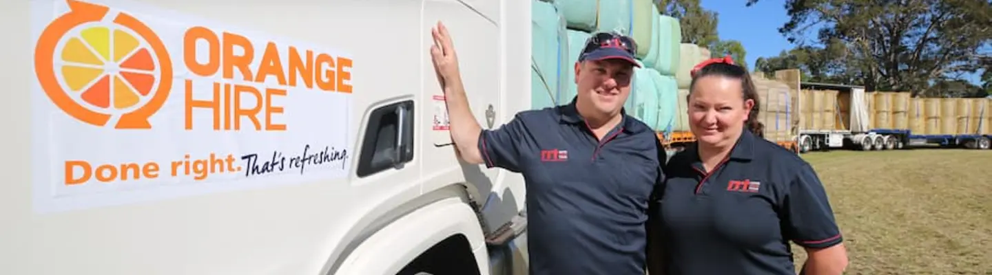Deux employés en uniforme debout à côté d’une rangée de camions chargés sur un chantier, surveillant les opérations de chargement et la sécurité.