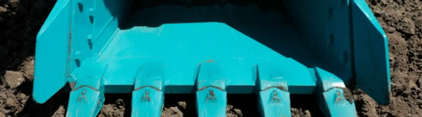 Rouleau à godet reposant sur du sable sur un chantier de construction, utilisé pour compacter le sol avec des barrières de sécurité en arrière-plan.