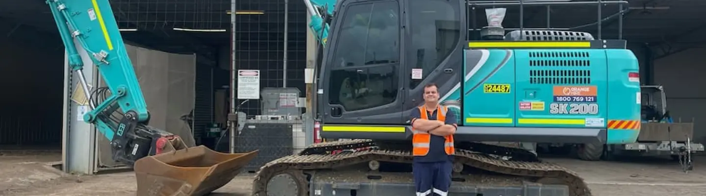 Un homme debout à côté d’une excavatrice près des barrières de sécurité installées sur un chantier.
