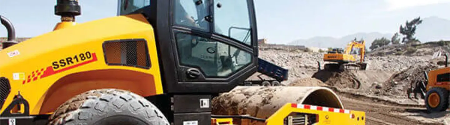 Hommes utilisant des machines lourdes sur un chantier de construction, entourés de barrières de sécurité et portant un équipement de protection.