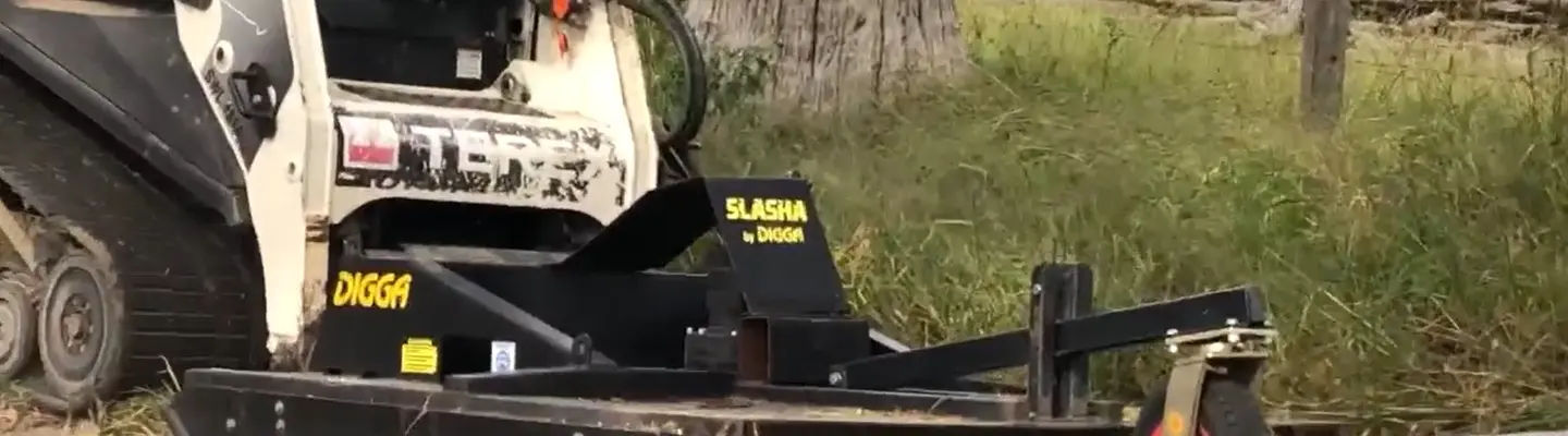 Machine de coupe positionnée dans un champ ouvert, utilisée pour couper l’herbe ou dégager la végétation près d’un chantier.