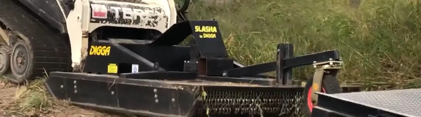 Une machine qui coupe l’herbe dans un champ ouvert, mettant en évidence l’entretien et la sécurité des terrains près des zones de construction.
