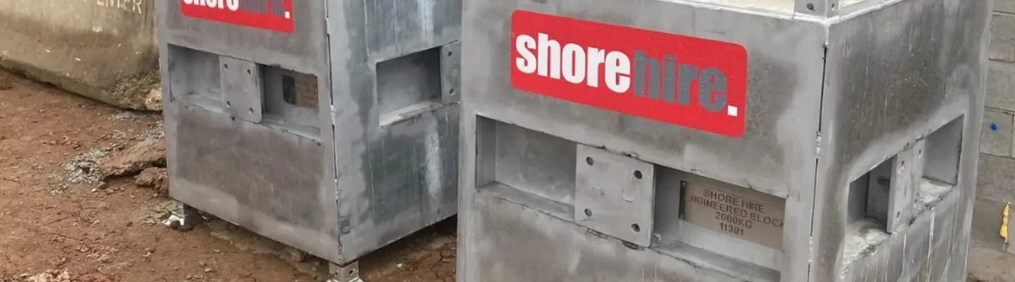 Travailleur installant un système de contrepoids en béton pour stabiliser les poteaux pendant un travail de levage sur un chantier de construction.
