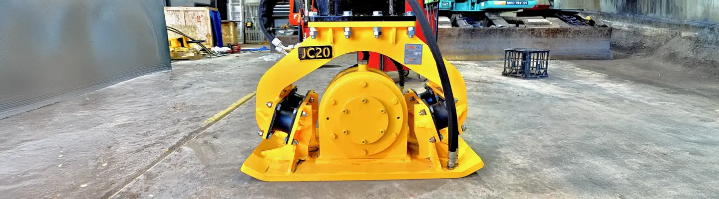 Machine de compactage à plaque sur un chantier de construction près de barrières de sécurité, utilisée pour compacter le sol et maintenir la stabilité du sol.