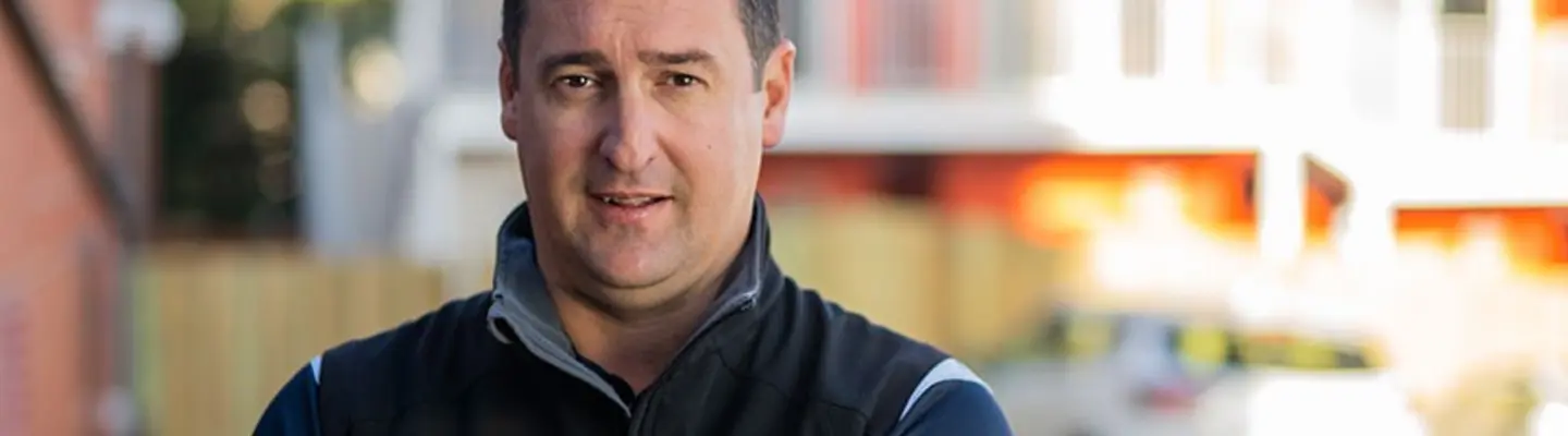 Un homme se tenant fièrement devant un conteneur d’expédition, représentant l’innovation dans la conception de logement modulaire et durable.