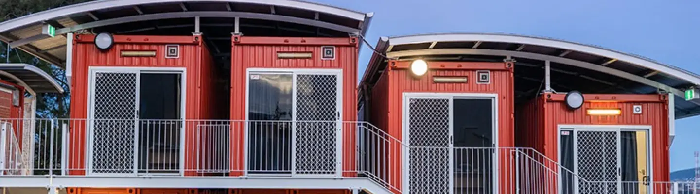 Unités de logement modulaires de deux étages fabriquées à partir de conteneurs d’expédition avec escaliers extérieurs et balcons au crépuscule.