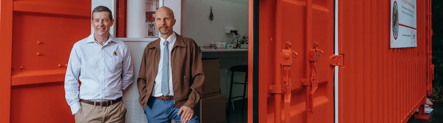 Deux hommes debout à côté d’un conteneur de bureau rouge ouvert avec un espace de travail intérieur visible.