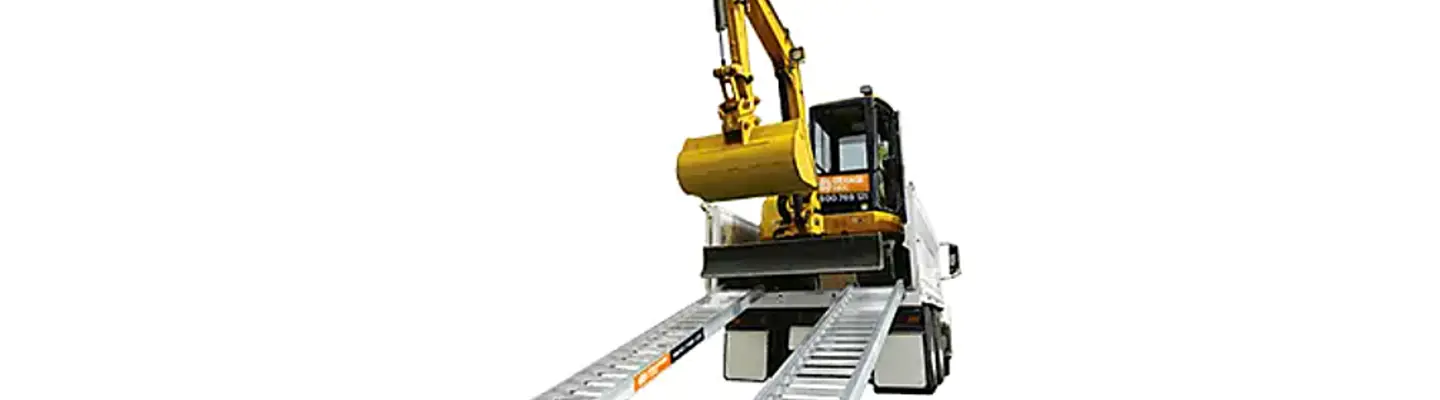 Une excavatrice compacte positionnée sur une rampe de remorque, prête à être chargée ou transportée sur un fond lisse.