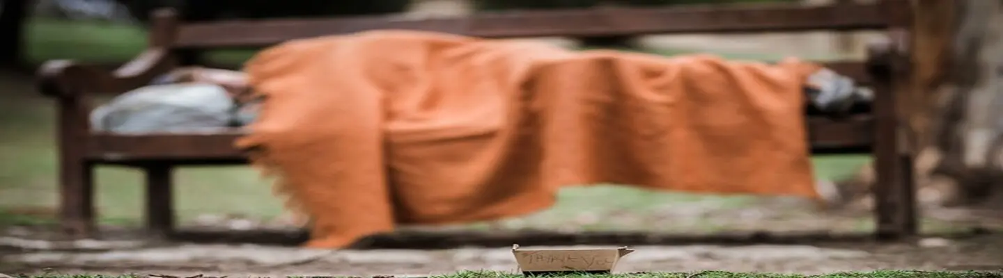 Homme sans abri dormant sur un banc dans un parc pendant la journée, soulignant la pauvreté urbaine et le besoin de solutions d’abri.