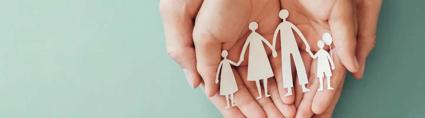 Mains tenant une découpe en papier d’une famille symbolisant l’attention et la protection.