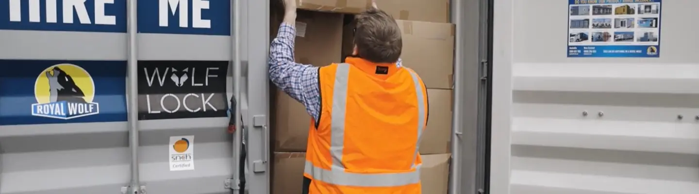 Travailleur dans un gilet haute visibilité chargeant des boîtes en carton dans un conteneur de stockage.