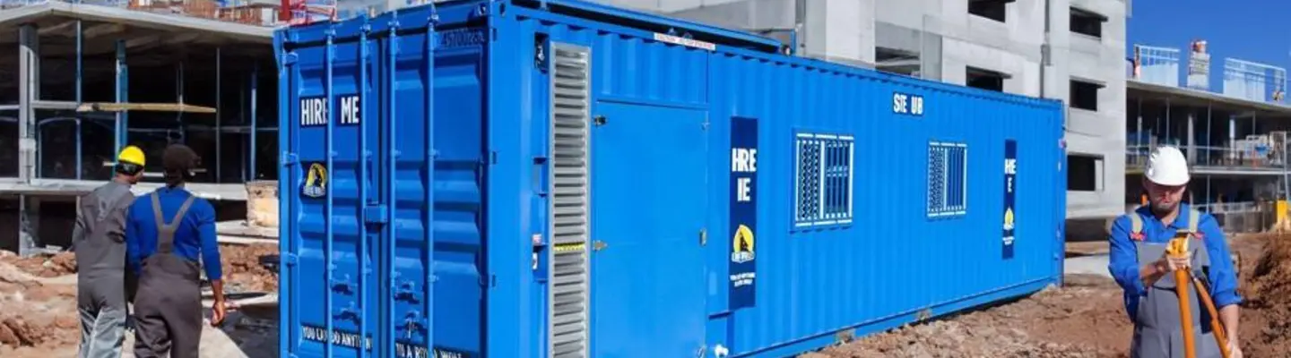 Un conteneur d’expédition bleu installé sur un chantier de construction avec des travailleurs à proximité.