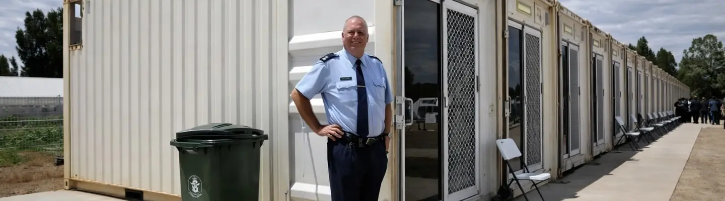Homme debout en toute confiance devant une maison conteneurisée moderne, présentant une conception de vie modulaire innovante.