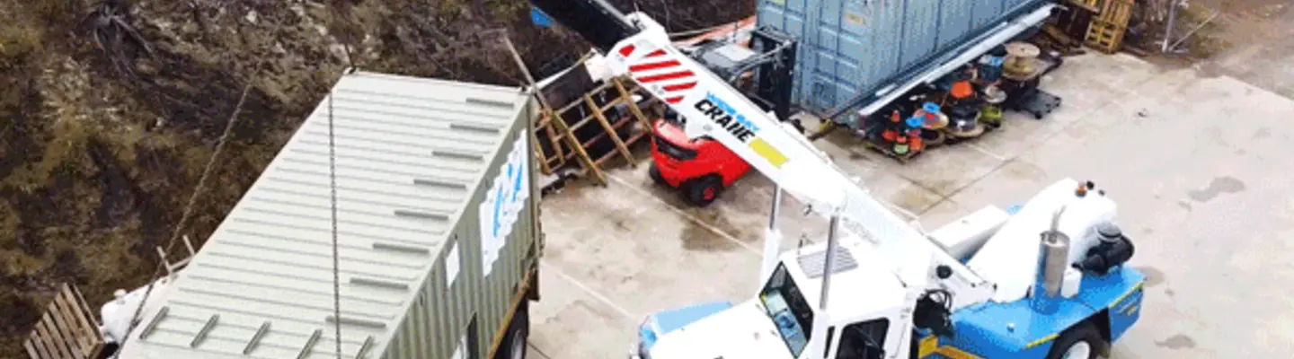 Conteneurs d’expédition empilés près de camions avec divers matériaux de construction, illustrant un site de logistique et de stockage très fréquenté.