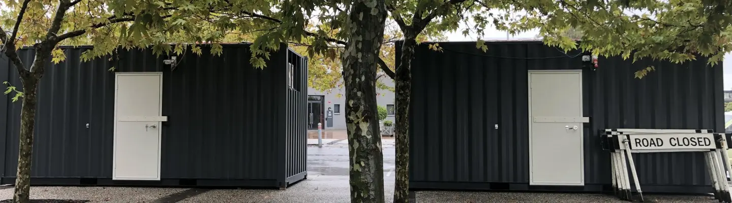 Caisson à billets fabriqué à partir d’un conteneur d’expédition réutilisé, doté de fenêtres de service et d’une signalisation dans un design compact et fonctionnel.