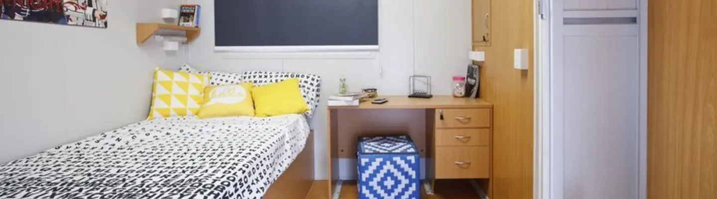 Chambre modulaire compacte avec lit simple, bureau, rangement et climatisation.