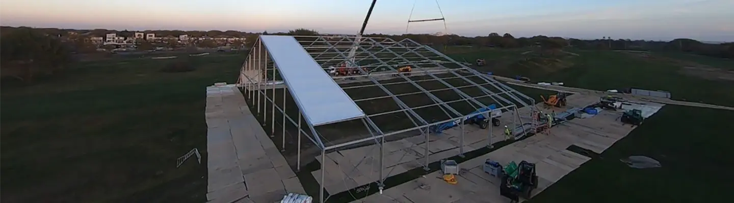 Installation d’un panneau de toiture sur une grande structure temporaire en toile à l’aide d’une grue au crépuscule dans un champ ouvert