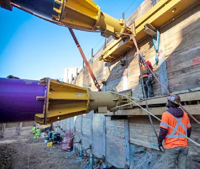 Intérieur de la tranchée excavée où un travailleur portant une veste réfléchissante regarde des jambes de force hydrauliques