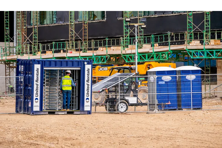 Un travailleur utilisant un tourniquet pour entrer sur un chantier à gauche et des toilettes portatives à droite.