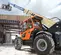 Vue latérale d’un chariot élévateur à portée variable JLG orange et jaune avec flèche allongée, chariot élévateur et cabine sur un chantier de construction.