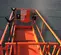 Vue du dessus d’une plateforme de godet d’élévateur à mât vertical orange avec des rails de sécurité sur les côtés.