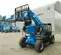 Vue avant inclinée d’un chariot élévateur à portée variable Genie bleu avec flèche et fourche allongées avec cabine ouverte sur un chantier de construction.