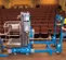 Vue latérale d’un kit d’échelle Genie bleu pour nacelle élévatrice avec bras rétracté, inactif sur une scène dans un auditorium.