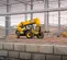 Vue avant inclinée d’un chariot élévateur à portée variable JCB jaune avec des palettes de levage de flèche rétractées de matériaux de construction sur un chantier.