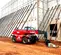 Vue latérale d’un chariot élévateur à portée variable Magni rouge avec cabine fermée et flèche rétractée sur un chantier de construction.