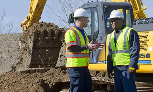 deux hommes portant un casque de sécurité sur un chantier de construction avec excavatrice 