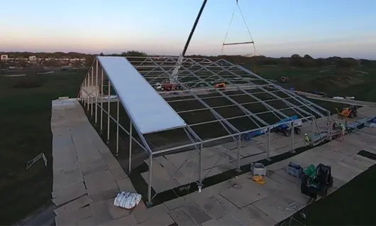 Installation d’un panneau de toiture sur une grande structure temporaire en toile à l’aide d’une grue au crépuscule dans un champ ouvert