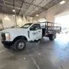 Vue du côté gauche, un camion à plateau blanc est stationné dans un grand garage ou un hall de service.
