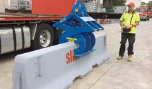 Worker observing as heavy machinery moves a concrete safety barrier into place on a roadway construction site.