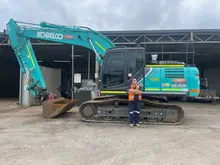 A man standing beside an excavator near installed safety barriers on a job site.