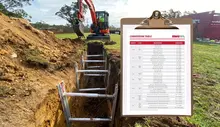 Construction machine near a trench with a conversion table displayed, aiding in accurate measurements and safe installation.