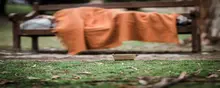 Homeless man sleeping on a bench in a park during the day, highlighting urban poverty and the need for shelter solutions.