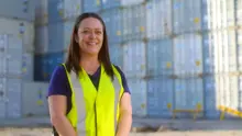 Company employee standing in front of a stack of shipping containers, used for storing and transporting construction safety barriers.